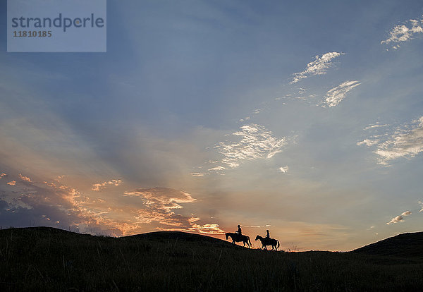 Silhouette eines kaukasischen Paares  das bei Sonnenuntergang auf Pferden reitet