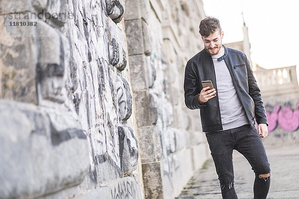 Lächelnder kaukasischer Mann  der auf dem Bürgersteig geht und eine SMS auf seinem Handy schreibt