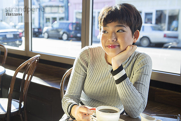 Nachdenkliches asiatisches Teenager-Mädchen trinkt Kaffee in einem Café