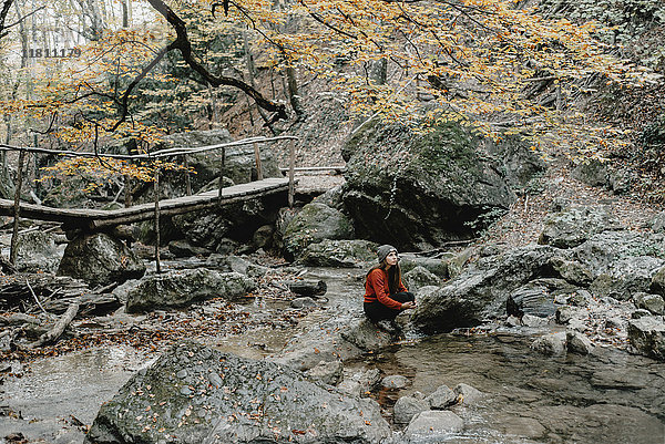 Kaukasische Frau sitzt auf einem Felsen im Bach