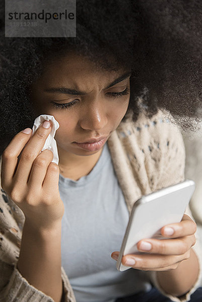 Afroamerikanische Frau weint und schreibt eine SMS auf ihrem Handy