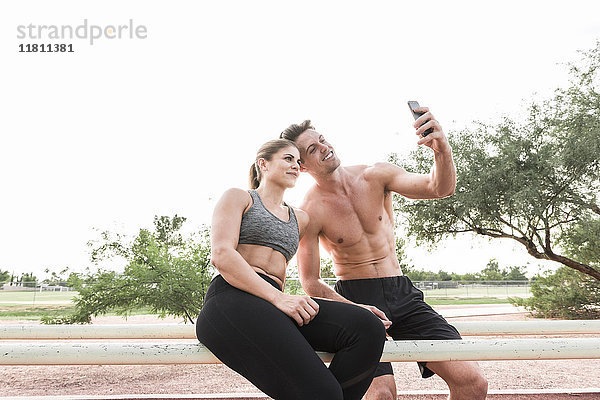 Paar  das auf einem Geländer sitzt und für ein Selfie mit dem Handy posiert