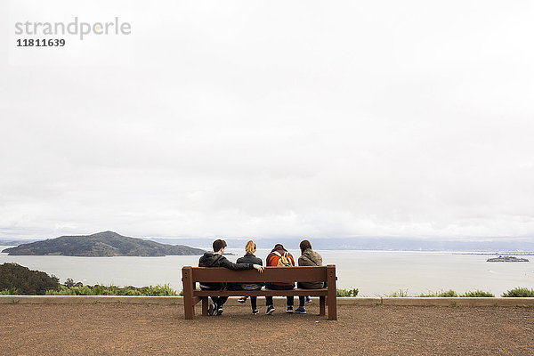 Freunde sitzen auf einer Bank und bewundern die schöne Aussicht auf das Meer