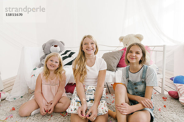 Porträt von lächelnden Schwestern aus dem Nahen Osten  die im Schlafzimmer auf dem Boden sitzen