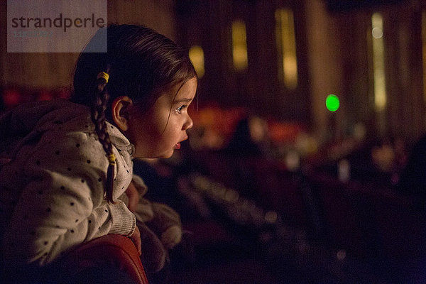 Gemischtrassiges Mädchen lehnt auf einem Stuhl und schaut einen Film im Kino