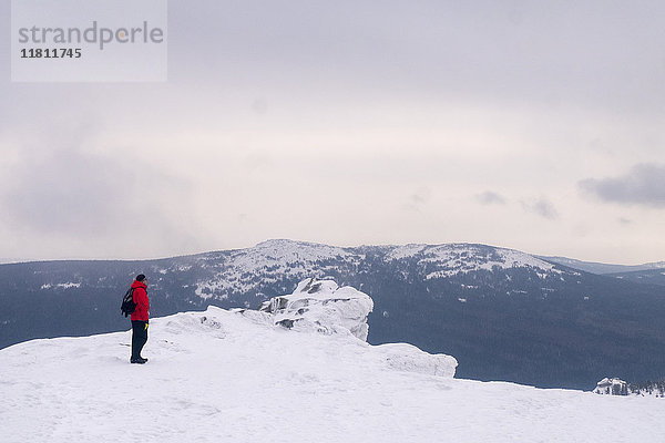 Kaukasischer Mann steht auf einem abgelegenen Berg im Winter