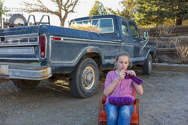 Kaukasisches Mädchen sitzt auf einem Stuhl in der Nähe eines Lastwagens und strickt