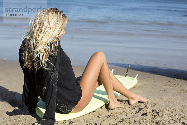 Kaukasische Frau sitzt auf einem Surfbrett am Strand