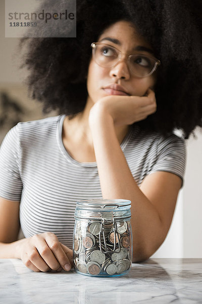 Nachdenkliche afroamerikanische Frau mit einem Krug voller Münzen