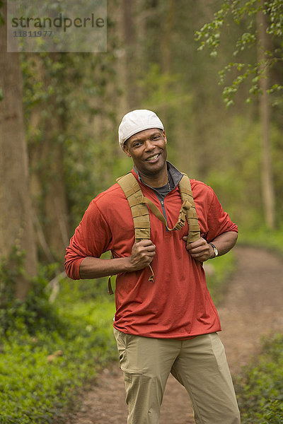 Afroamerikanischer Mann steht auf einem Pfad im Wald und trägt einen Rucksack