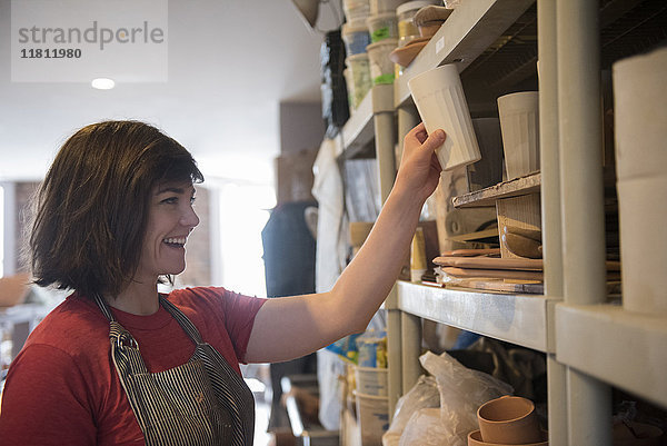 Lächelnde kaukasische Frau stellt Tasse auf Regal in Werkstatt