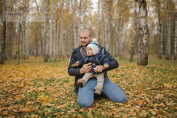 Vater aus dem Nahen Osten kniet im Park mit seinem kleinen Sohn im Herbst