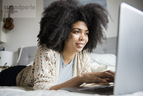 Afroamerikanische Frau liegt im Bett und benutzt einen Laptop