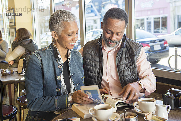 Gemischtrassiges Paar beim Lesen eines Reiseführers in einem Café
