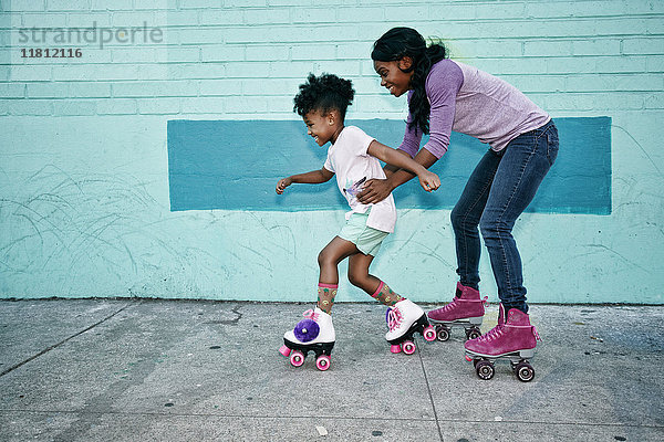 Schwarze Mutter hält die Taille ihrer Tochter in Rollschuhen