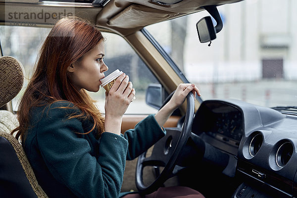 Kaukasische Frau fährt Auto und trinkt Kaffee