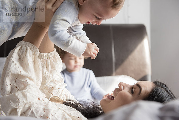 Kaukasische Mutter liegt auf dem Bett und hebt ihren kleinen Sohn hoch