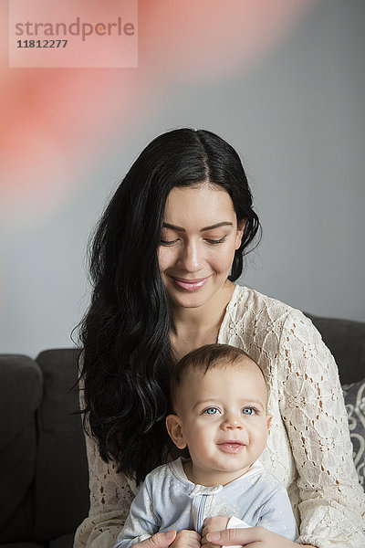 Kaukasische Mutter hält lächelnd Baby Sohn im Schoß