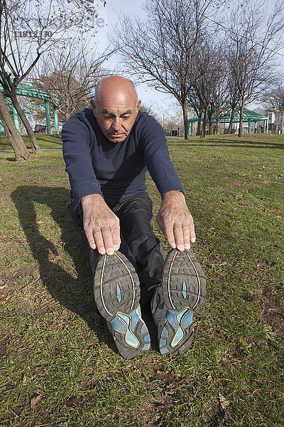 Hispanischer Mann sitzt auf Gras im Park und streckt die Beine aus