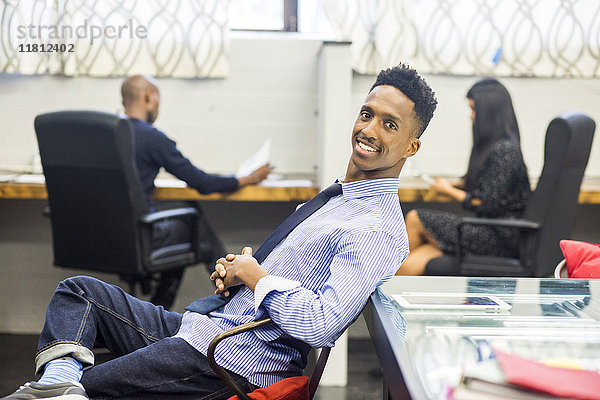 Porträt eines lächelnden schwarzen Mannes  der sich im Büro entspannt