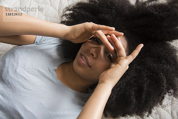 Eine afroamerikanische Frau liegt im Bett und hält sich die Augen zu