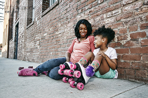 Schwarze Mutter und Tochter mit Rollschuhen auf dem Bürgersteig sitzend