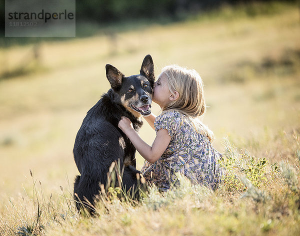 Kaukasisches Mädchen sitzt auf einem Feld und küsst einen Hund