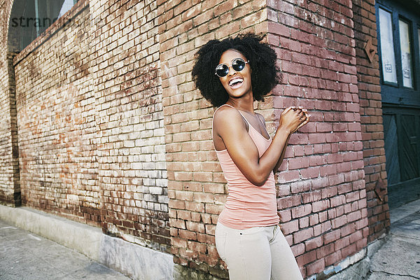 Lachende schwarze Frau  die in der Nähe der Ecke eines Backsteingebäudes steht