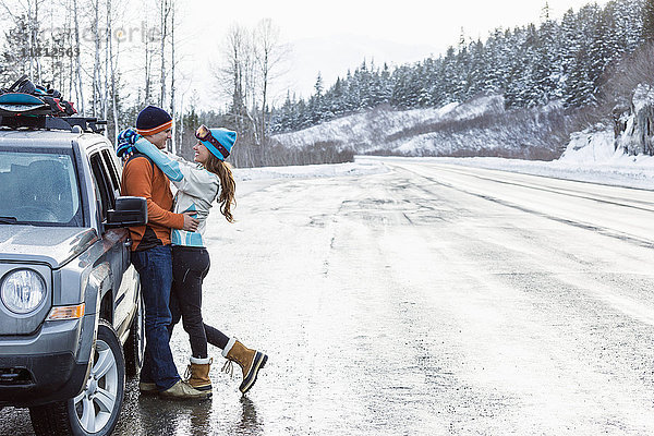 Kaukasisches Paar umarmt in der Nähe von Auto im Winter