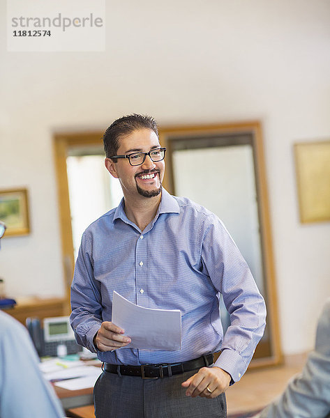 Lächelnder hispanischer Geschäftsmann  der Papierkram im Büro hält