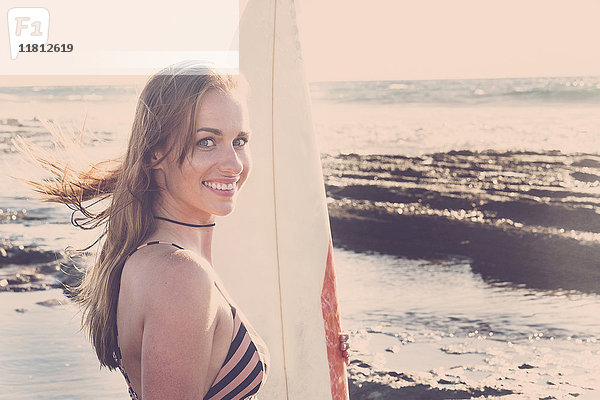 Kaukasische Frau steht am Strand und hält ein Surfbrett