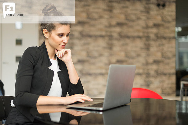 Junge Geschäftsfrau betrachtet Laptop auf Bürotisch