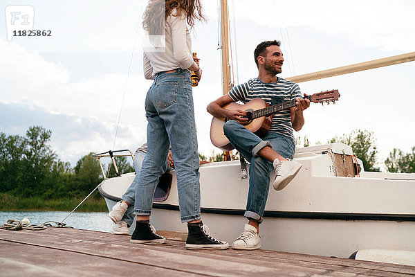 Drei Freunde entspannen sich am Pier  sitzen auf einem Segelboot  Mann spielt Gitarre