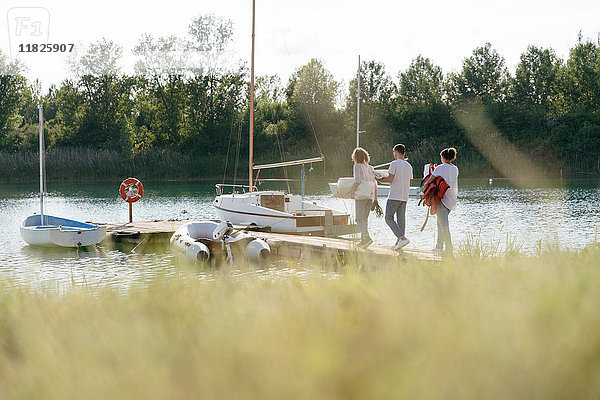 Freunde gehen auf ein Segelboot zu  Ausrüstung tragend  langes Gras im Vordergrund