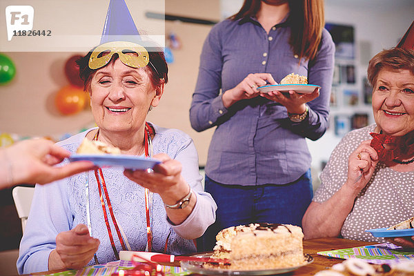 Ältere Frauen bekommen auf einer Party Geburtstagskuchen serviert