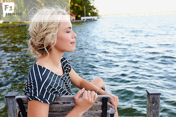 Frau sitzt auf Pier am Wasser