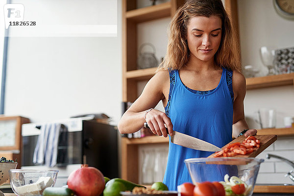 Junge Frau am Küchentisch schneidet Tomaten