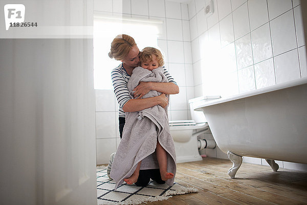 Mutter und Tochter im Badezimmer  Mutter wickelt die Tochter in ein Badetuch und umarmt sie