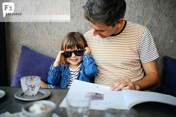 Mädchen spielt mit der Sonnenbrille des Vaters im Café