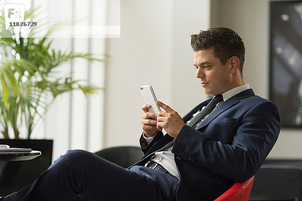 Geschäftsmann sitzt im Büro und schaut auf sein Smartphone