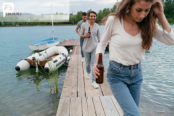 Drei Freunde gehen am Pier entlang und halten Flaschenbier