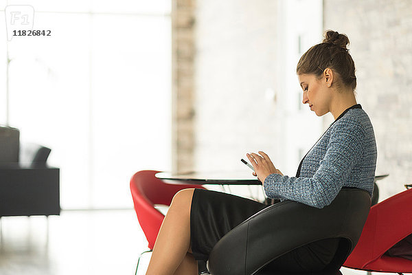 Geschäftsfrau sitzt im Büro und schaut auf ihr Smartphone