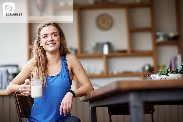 Junge Frau am Küchentisch mit Smoothie