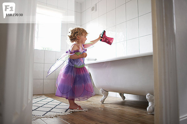 Junges Mädchen in Feenkostüm  hält Gummistiefel über die Badewanne