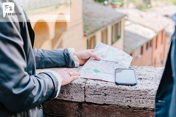 Ausschnittaufnahme eines Touristenpaares  das eine Karte an der Wand betrachtet  Siena  Toskana  Italien