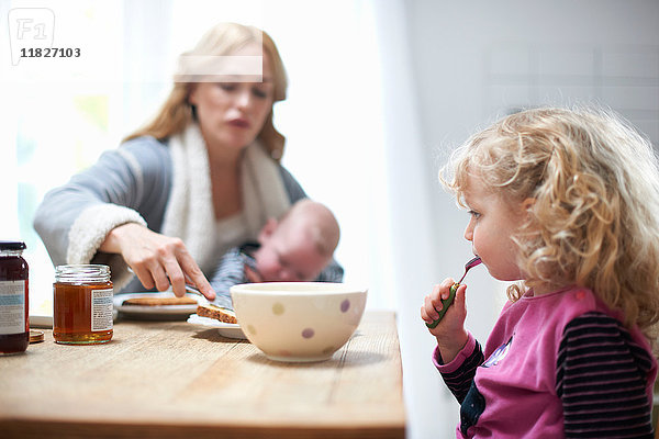Mutter  die einen kleinen Jungen hält  mit der kleinen Tochter am Küchentisch sitzt und frühstückt
