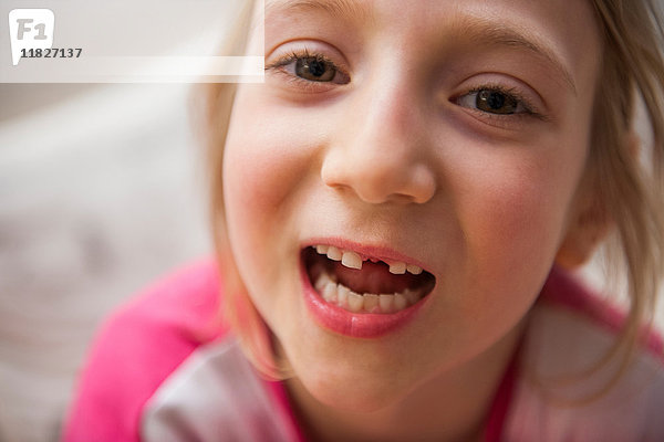 Porträt eines Mädchens mit fehlendem Zahn  das in den geöffneten Kameramund blickt