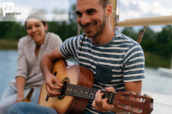 Mann und Frau entspannen sich auf einem vertäuten Segelboot  Mann spielt Gitarre