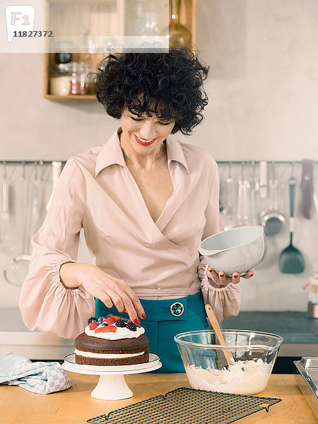 Frau dekoriert Schokoladenkuchen mit Milchcreme und frischen Sommerfrüchten
