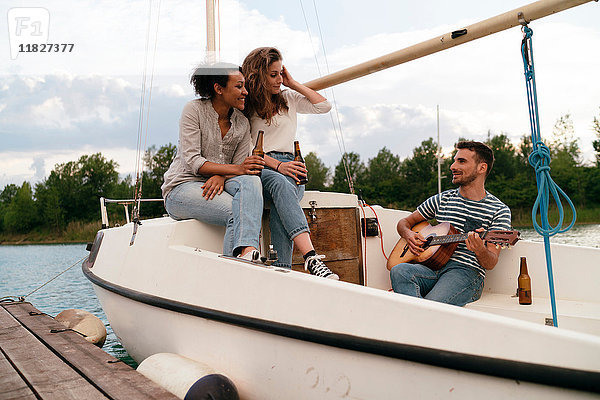 Drei Freunde entspannen sich auf einem vertäuten Segelboot  trinken Bier  Mann spielt Gitarre